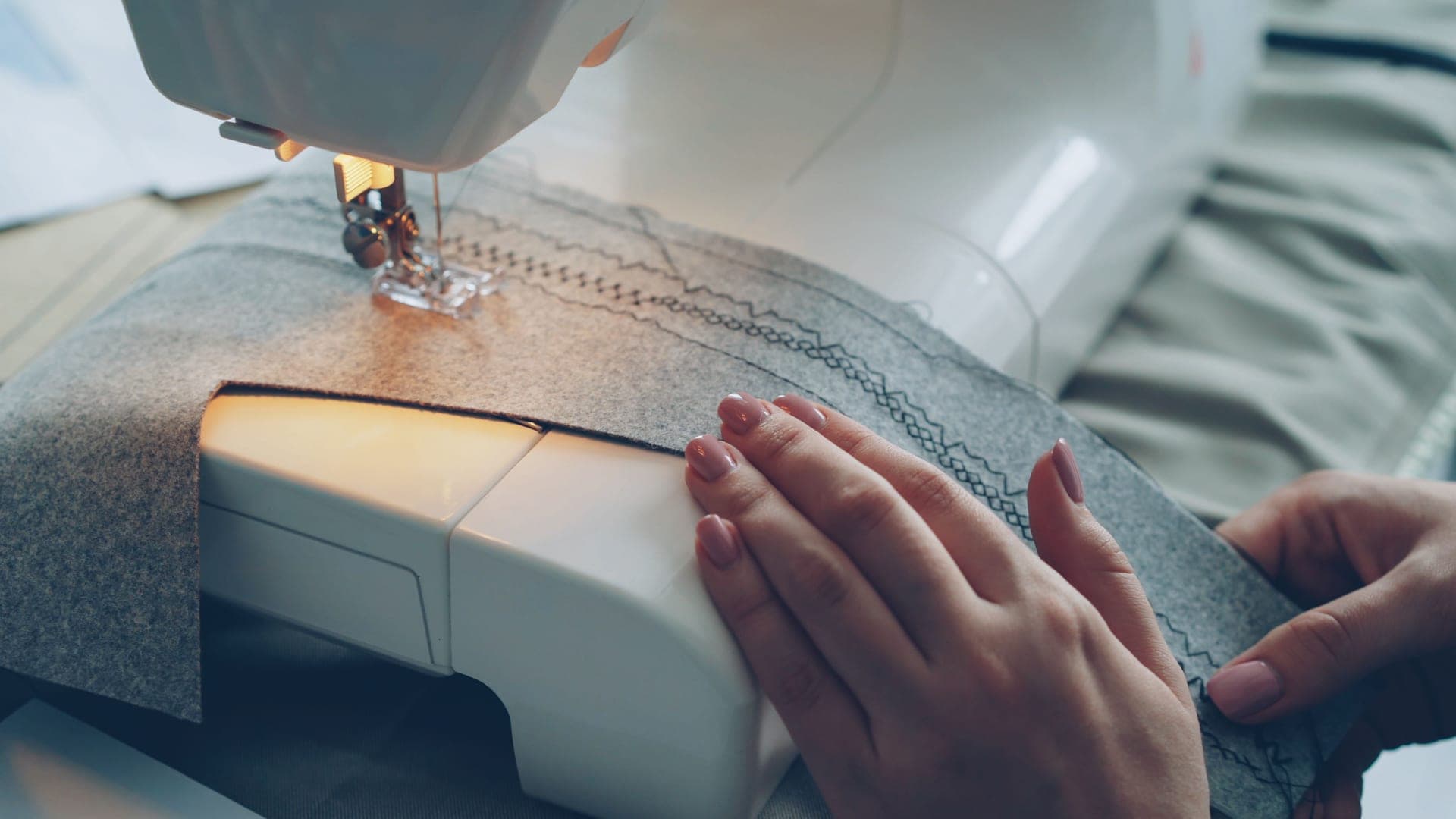Hands guiding fabric through a sewing machine as it stitches